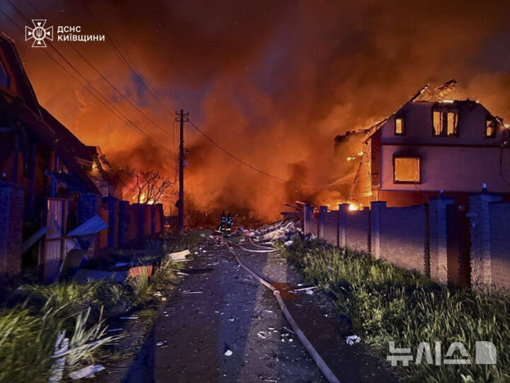 불길에 휩싸인 주택가에서 소방관들이 화재를 진압하고 있는 모습. 도로에는 소방호스와 잔해가 흩어져 있다.