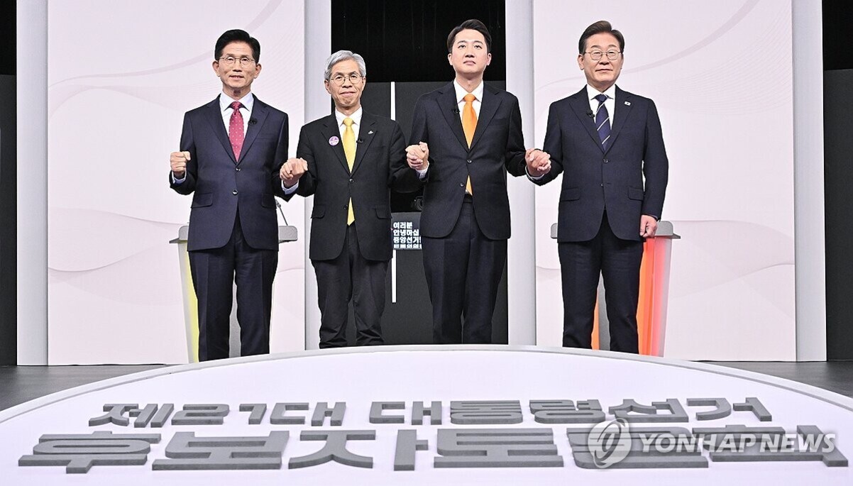 정장 차림의 네 명의 남성이 무대 위에 나란히 서서 손을 맞잡고 있다. 앞쪽에는 '제20대 대통령선거 후보자 토론회'라는 글자가 보인다.