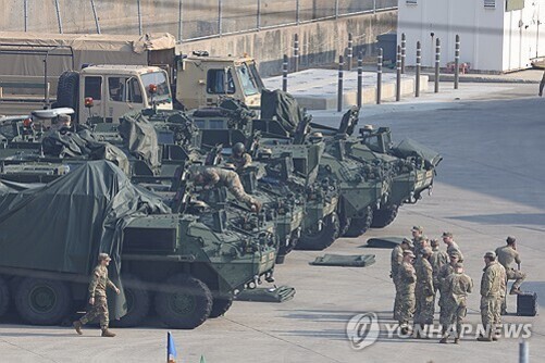 여러 대의 군용 차량과 그 주변에 모여 있는 군인들, 일부는 차량 위에서 작업 중임.
