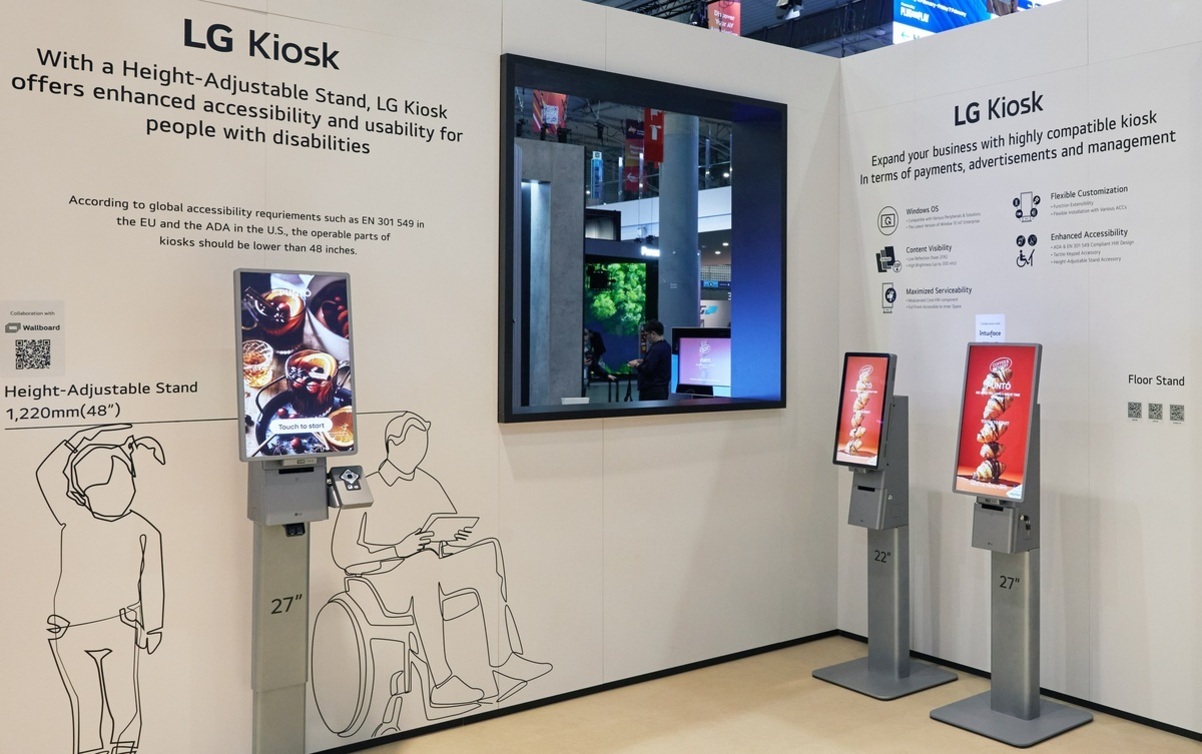 LG Kiosk 전시 부스에서 높이 조절이 가능한 키오스크와 일반 키오스크 두 대가 나란히 진열되어 있다. 벽면에는 접근성 향상 및 장애인 사용 편의성을 강조하는 설명과 함께 휠체어를 탄 사람과 어린이 일러스트가 그려져 있다.