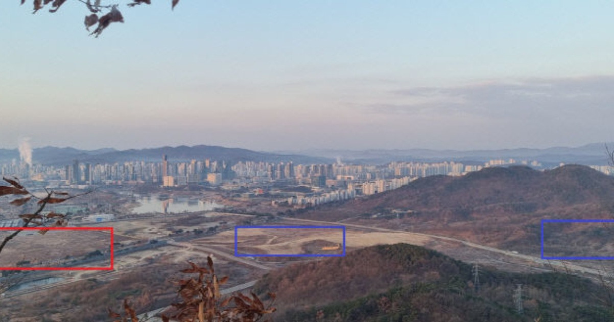 도시 외곽의 산과 평지, 멀리 고층 아파트 단지가 보이며, 전경에는 빨간색과 파란색 사각형으로 표시된 구역이 있다.