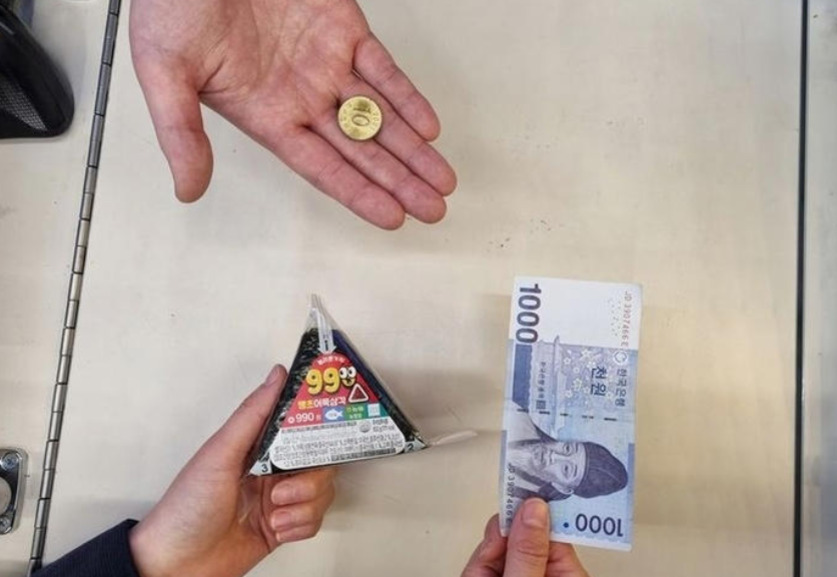 한 손에는 500원짜리 동전이, 다른 손에는 삼각김밥과 1,000원 지폐가 들려 있는 모습