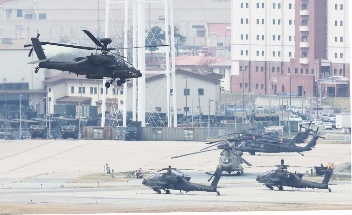 헬리콥터 여러 대가 군 기지 활주로에 정박해 있고, 한 대는 이륙 중이다. 배경에는 건물과 차량들이 보인다.