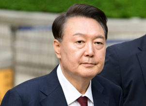 정장을 입은 중년 남성이 바깥에서 정면을 바라보고 있다.