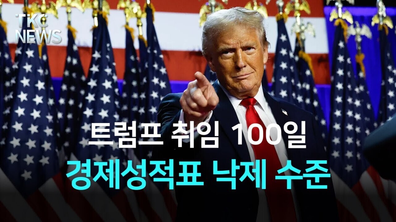 미국 국기와 성조기가 배경에 있는 무대에서 한 남성이 정면을 바라보며 손가락으로 앞을 가리키고 있다. 화면에는 '트럼프 취임 100일 경제성적표 낙제 수준'이라는 한국어 자막이 있다.