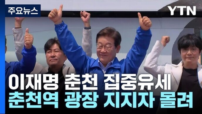 여러 명의 남성이 무대 위에서 파란색 옷을 입고 두 팔을 들어 올리며 환호하는 모습. 화면 왼쪽 상단에는 '주요뉴스'라는 글자가 있고, 오른쪽 상단에는 YTN 로고가 있다. 하단에는 '이재명 춘천 집중유세 춘천역 광장 지지자 몰려'라는 자막이 있다.