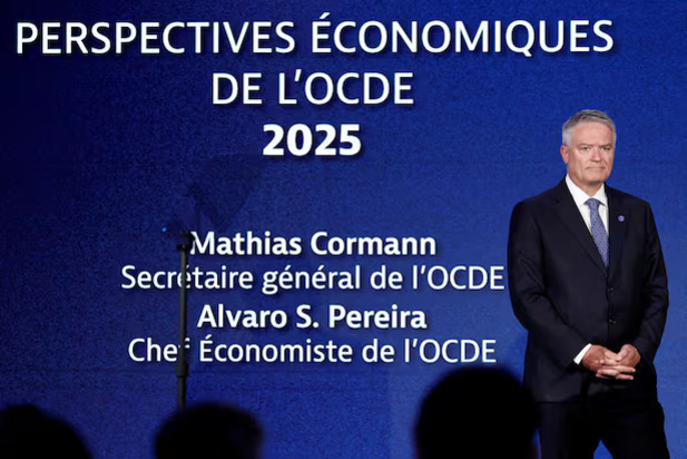 파란색 배경 앞에 정장을 입은 남성이 서 있고, 배경에는 'PERSPECTIVES ÉCONOMIQUES DE L'OCDE 2025', 'Mathias Cormann Secretaire général de l'OCDE', 'Alvaro S. Pereira Chef Économiste de l'OCDE'라는 프랑스어 문구가 적혀 있다.