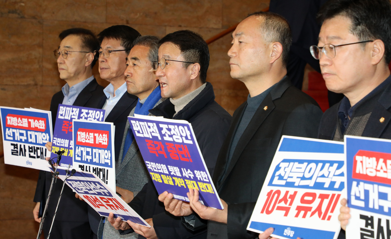 여러 명의 남성들이 일렬로 서서 피켓을 들고 항의하는 모습. 피켓에는 '지방소멸 가속화 선거구 대개악 결사 반대', '편파적 조정안 즉각 중단', '전북의석수 10석 유지' 등의 문구가 적혀 있다.