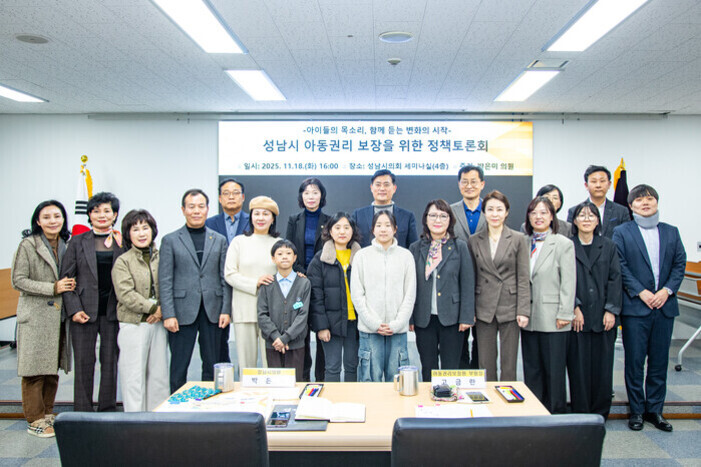 여러 명의 남성과 여성, 어린이들이 회의실에서 단체로 서서 사진을 찍고 있다. 뒤에는 '성남시 아동권리 보장을 위한 정책토론회'라는 현수막이 걸려 있다.