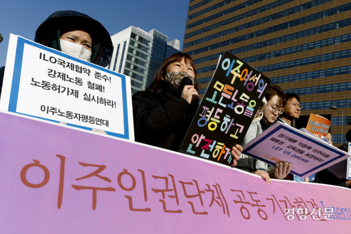 여러 명의 사람들이 도심에서 '이주인권단체 공동 기자회견'이라는 현수막을 들고 시위하고 있다. 참가자들은 이주노동자 권리 보장, 강제노동 철폐, 노동허가제 실시 등을 요구하는 피켓을 들고 있다.