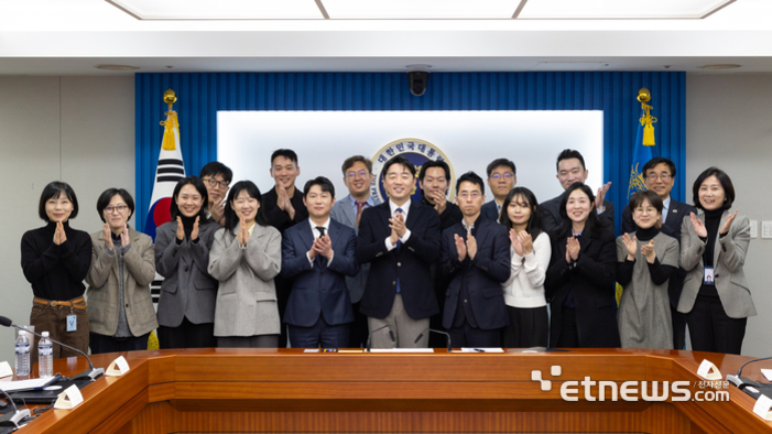 회의실에서 정장을 입은 남녀 여러 명이 단체로 서서 박수를 치고 있는 모습
